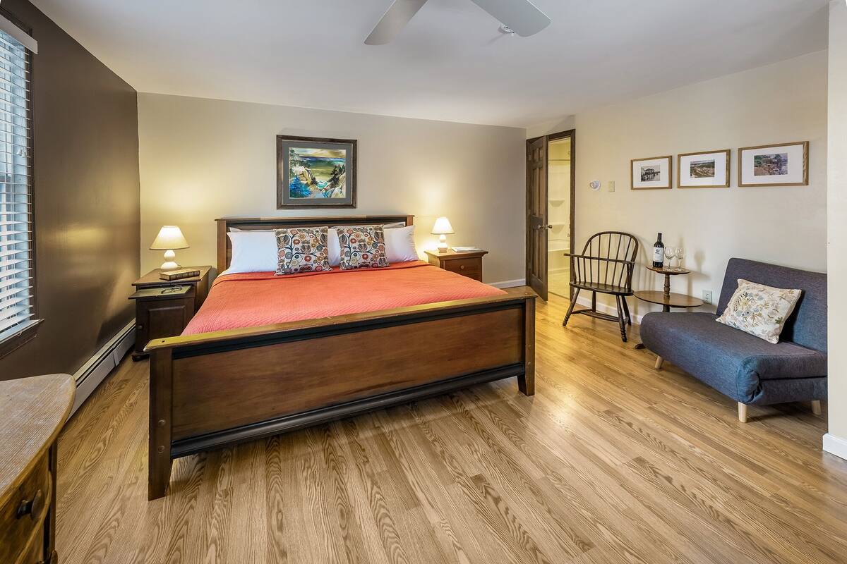 A bedroom with a wooden bed, a nightstand, a chair, a sofa, and a small table with a bottle and glasses.