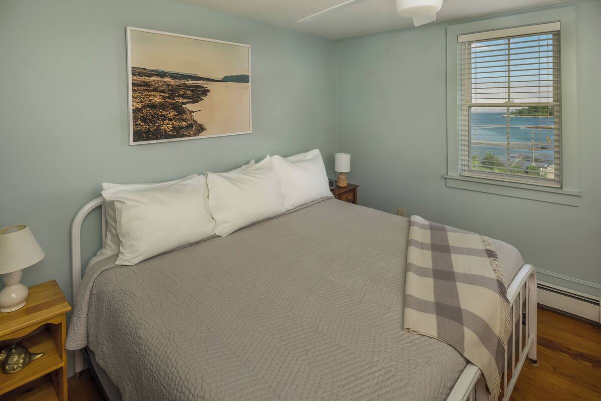 A neatly made bed with a quilt, a bedside lamp, and a framed picture on the wall.