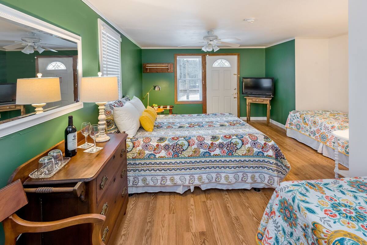 A bedroom with a large bed, a TV, a desk with a lamp, and a chair.