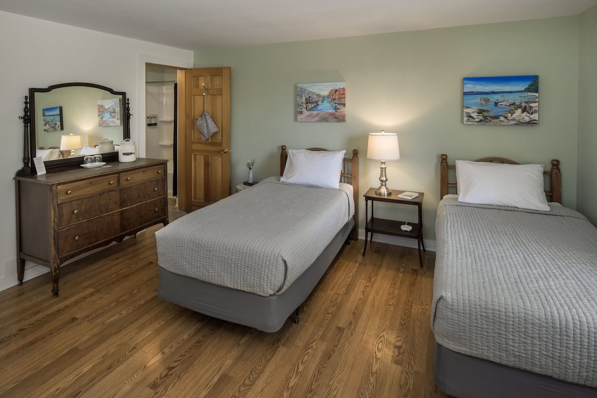 A bedroom with two beds, a dresser, a mirror, and artwork on the walls.