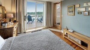 Une chambre à coucher avec un grand lit, une commode en bois, une table de chevet, une lampe, une fenêtre avec des rideaux, un ventilateur de plafond et une vue sur l’extérieur.