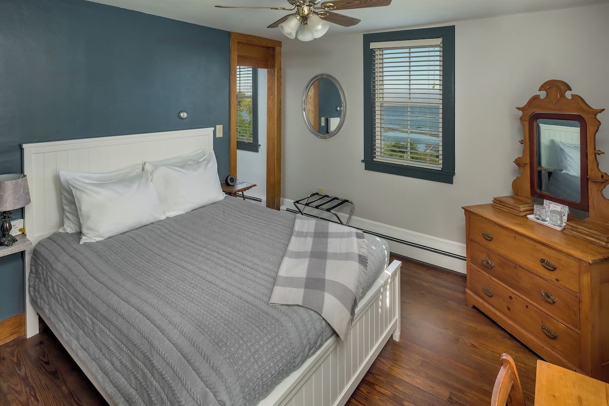A bedroom with a bed, dresser, mirror, and window with blinds.