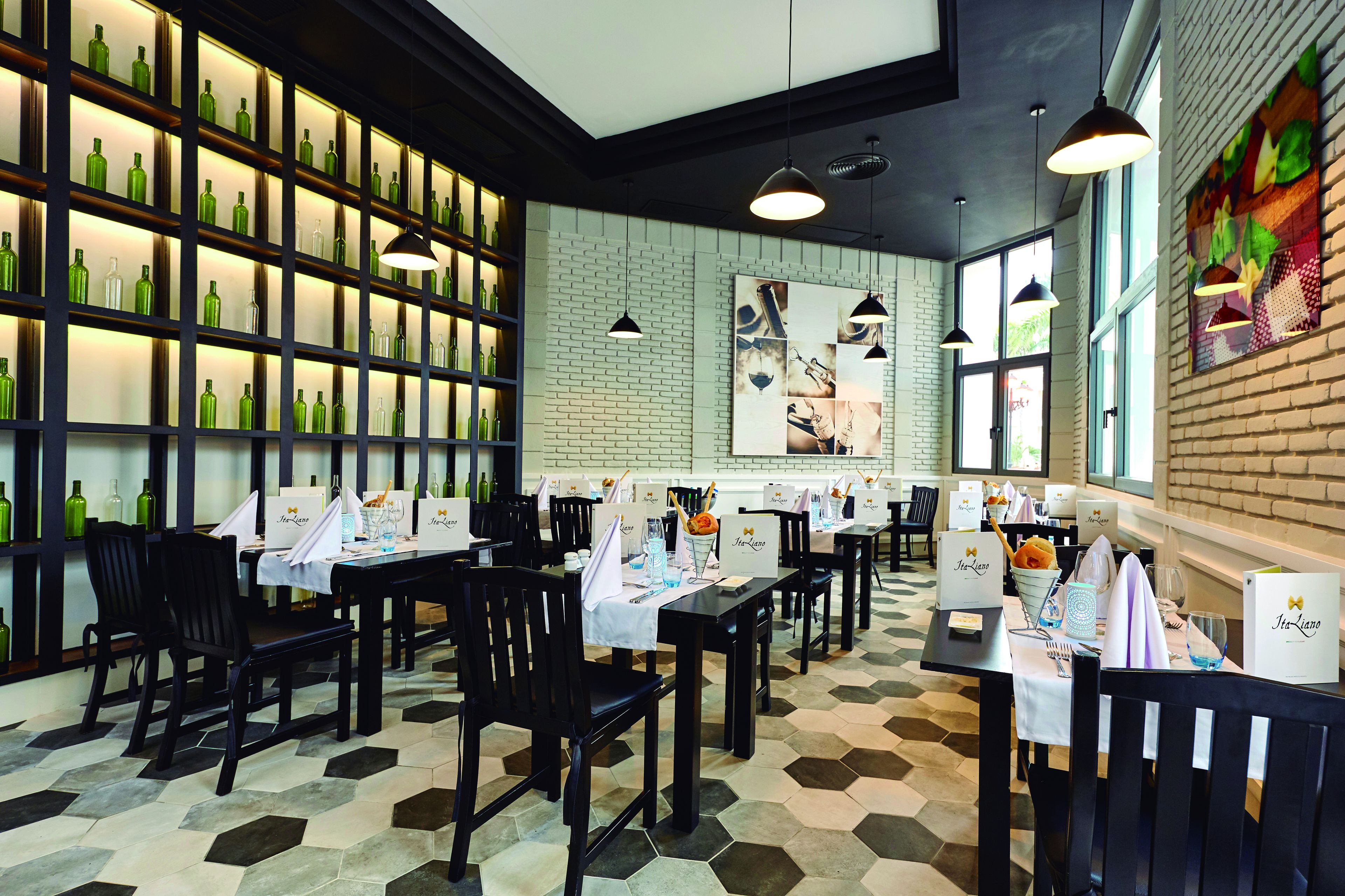 A restaurant with multiple tables set for dining, a brick wall, and shelves with green bottles.