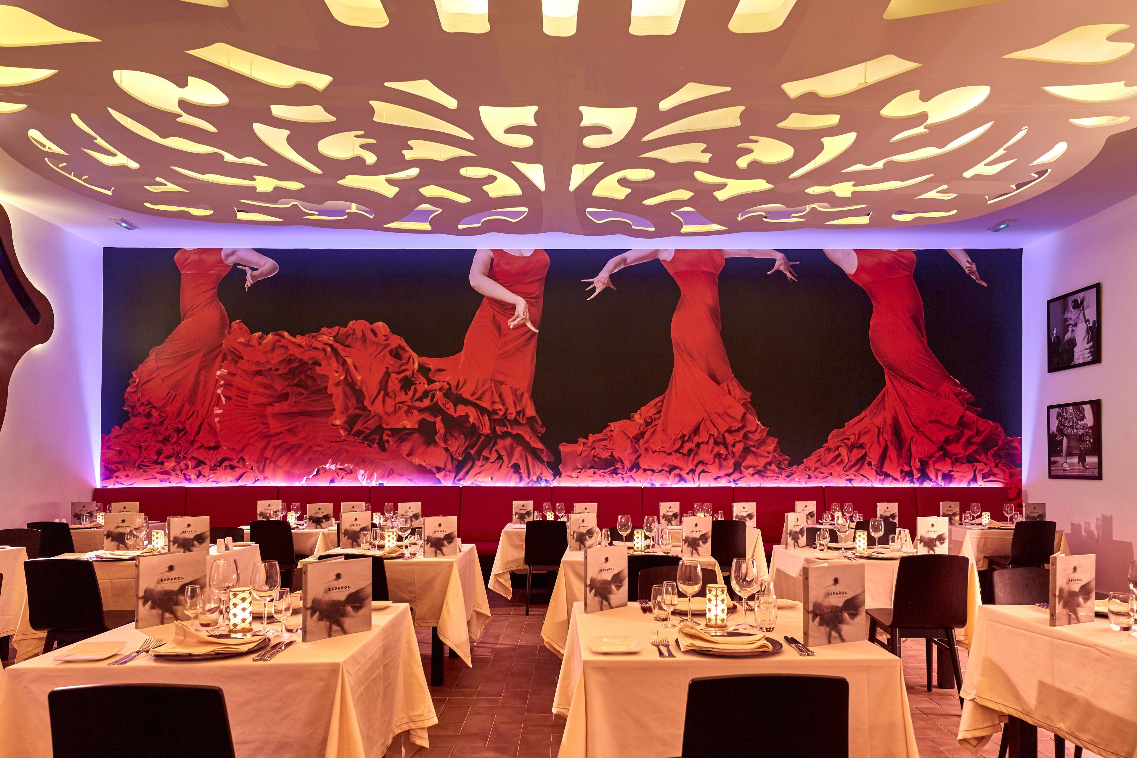 A restaurant with tables set for dining, featuring a large wall mural and modern ceiling design.