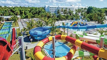 A water park with multiple slides and pools, surrounded by palm trees and a hotel in the background.