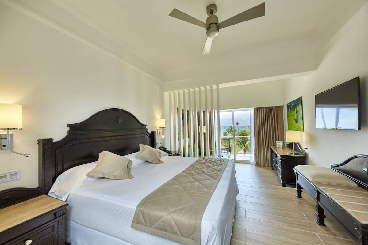 A hotel room with a large bed, a desk, a chair, a ceiling fan, and a view of the outdoors.