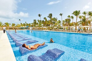 A swimming pool with lounge chairs, palm trees, and umbrellas.