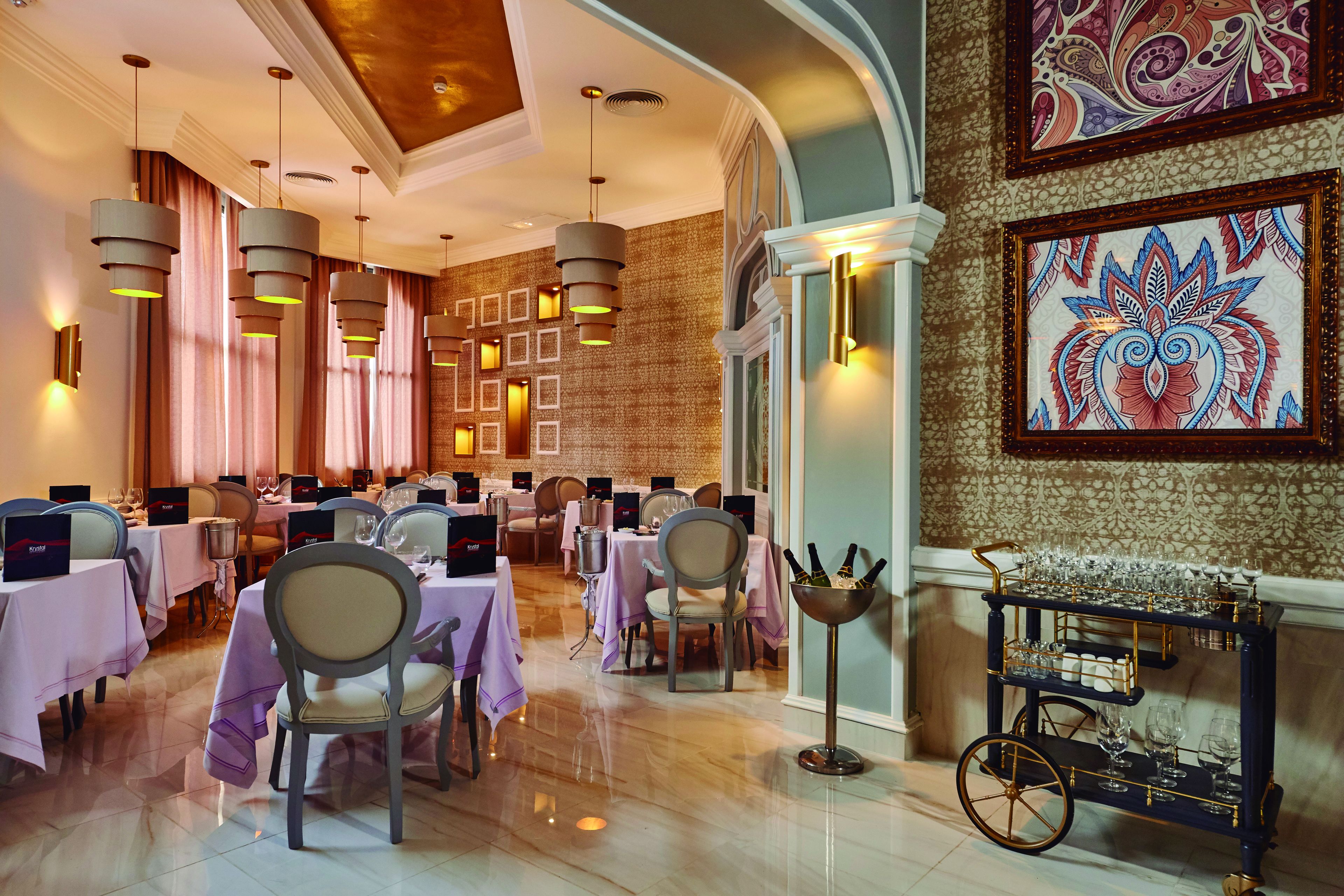 A dining area with tables set for a meal, a wine cart, and a decorative wall.