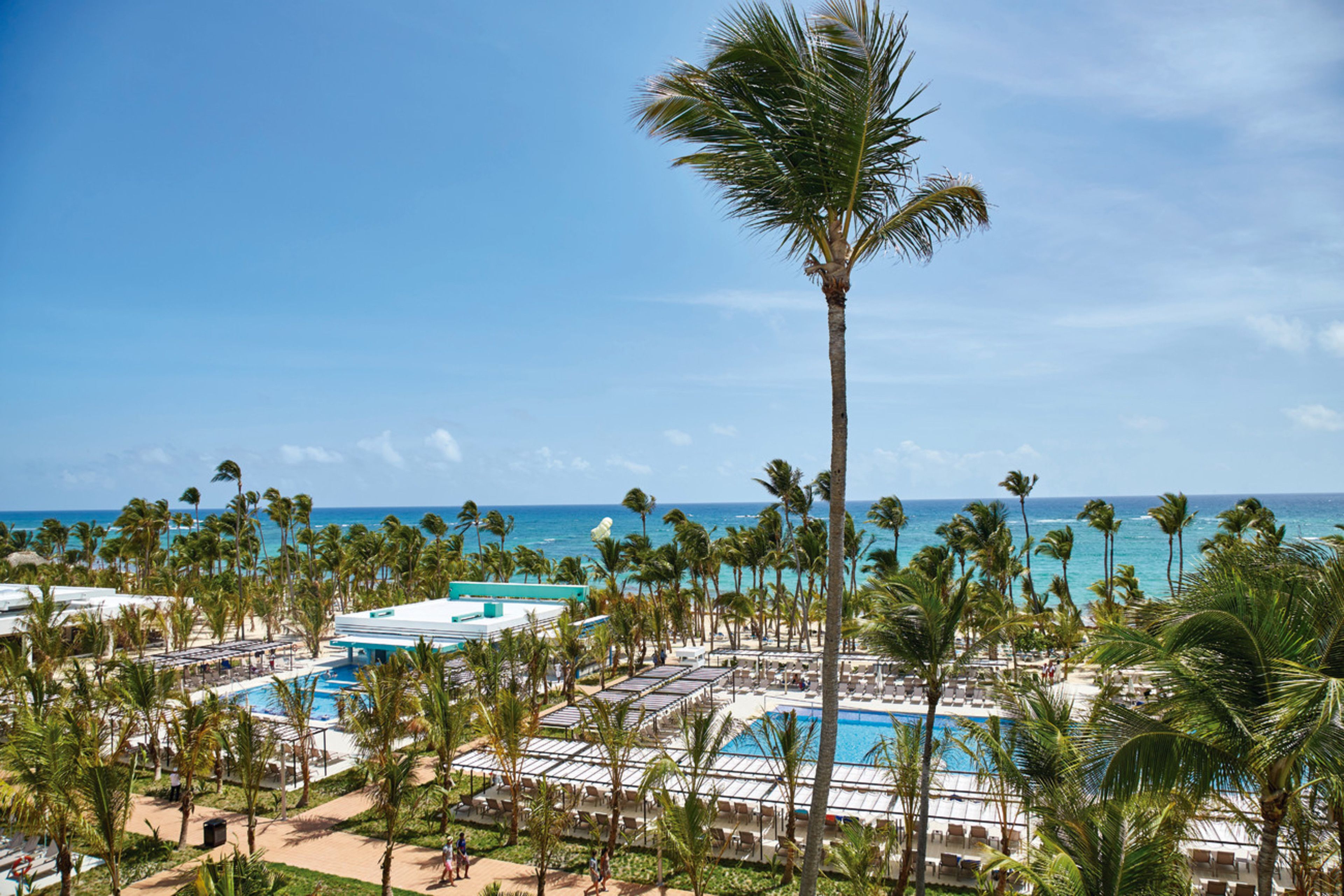 A resort with a pool area, palm trees, and a view of the ocean.