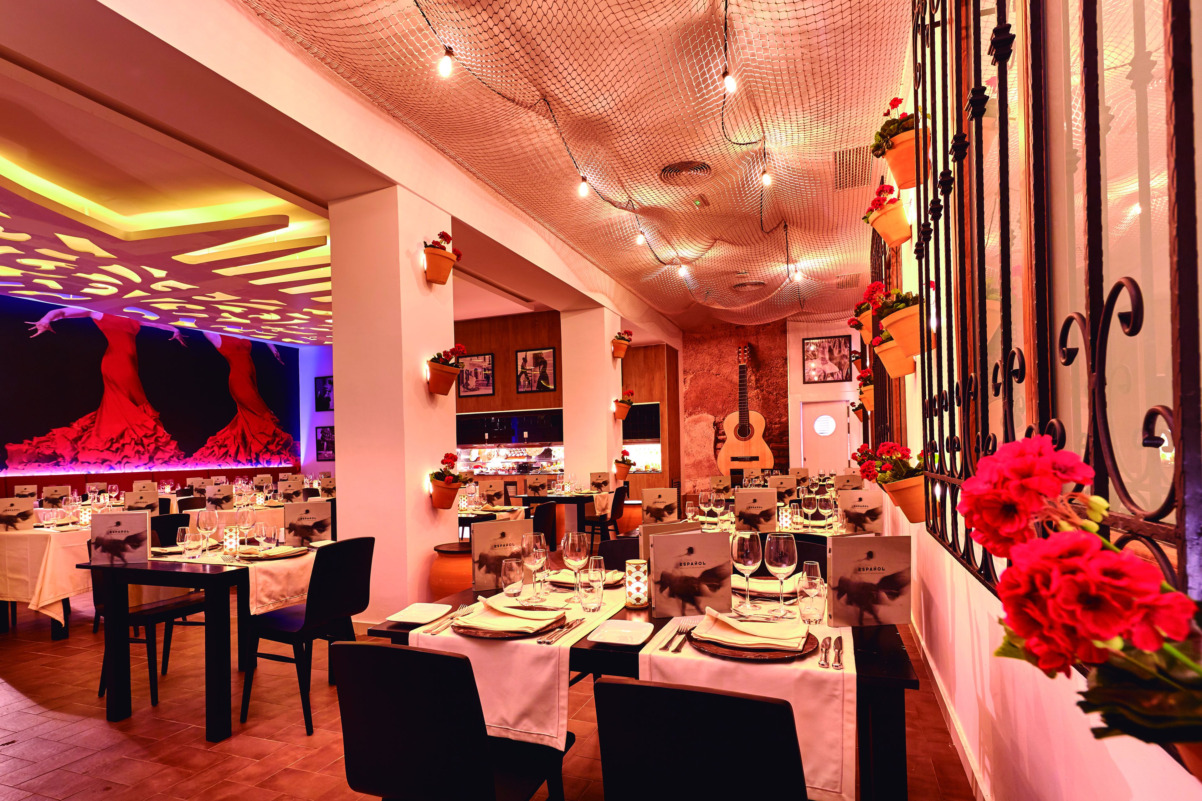 A restaurant with tables set for dining, a decorative ceiling, and hanging flower baskets.