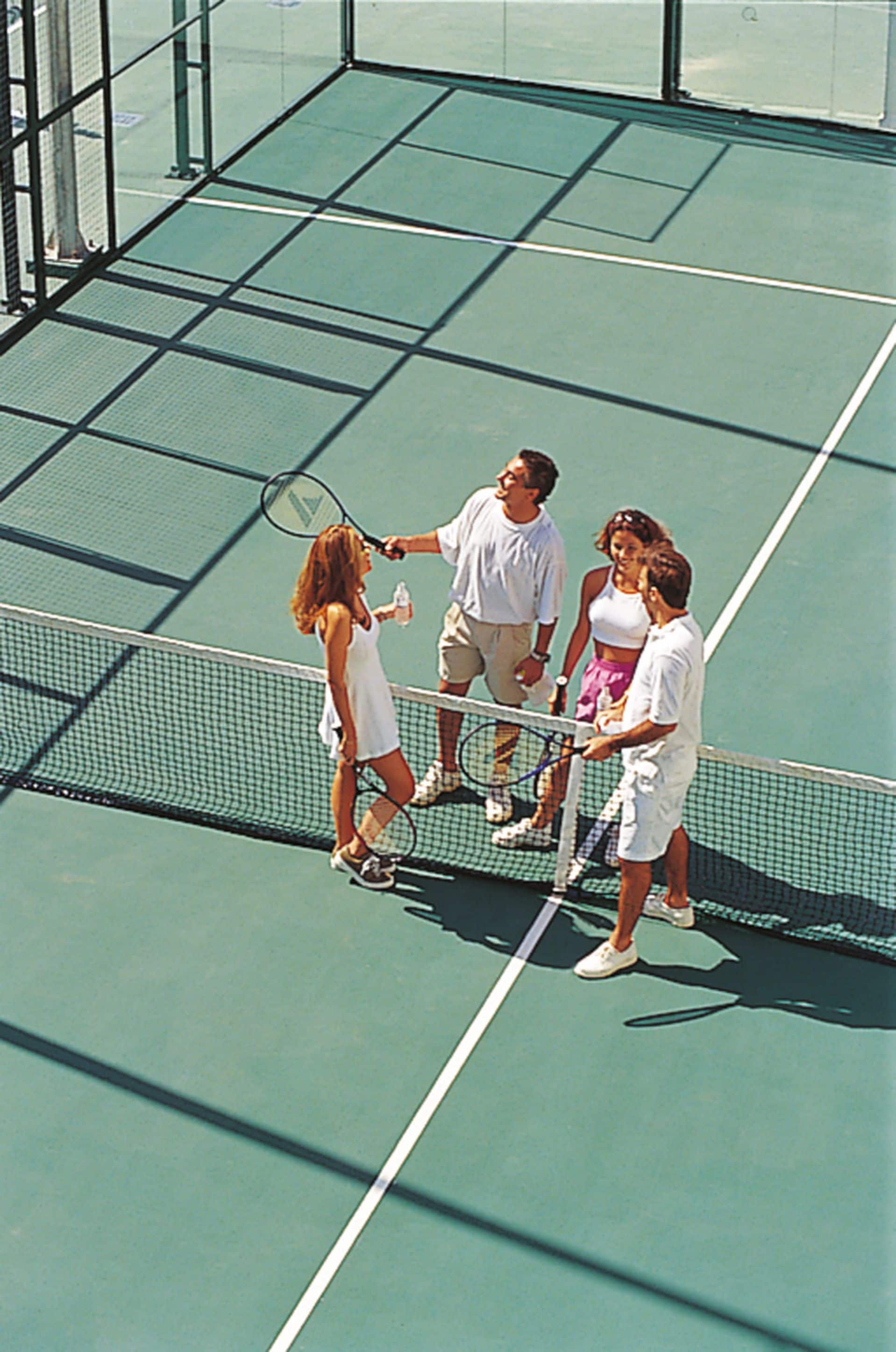 A tennis court with a net, three people, and a green surface.