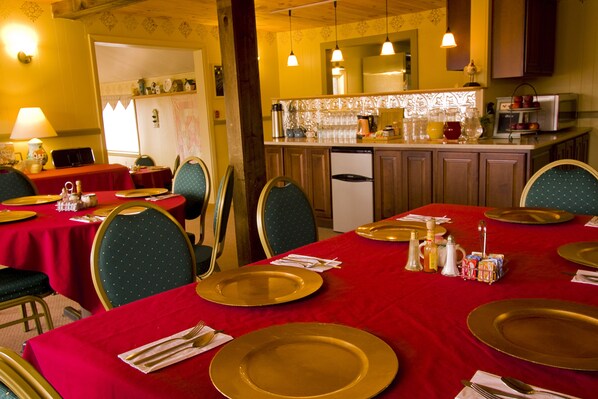A dining area with red tablecloths, gold-rimmed plates, and green chairs.