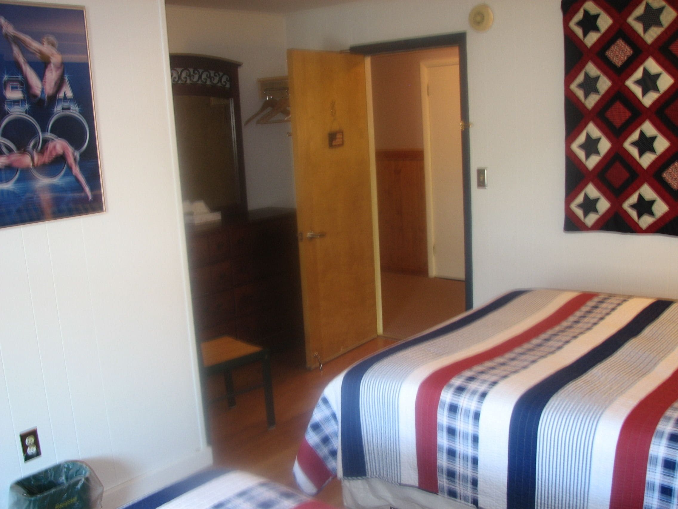 A bedroom with a bed, a wooden door, a mirror, and a wall with a patterned textile.