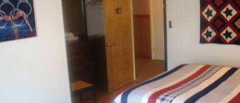 A bedroom with a bed, a wooden door, a mirror, and a wall with a patterned textile.