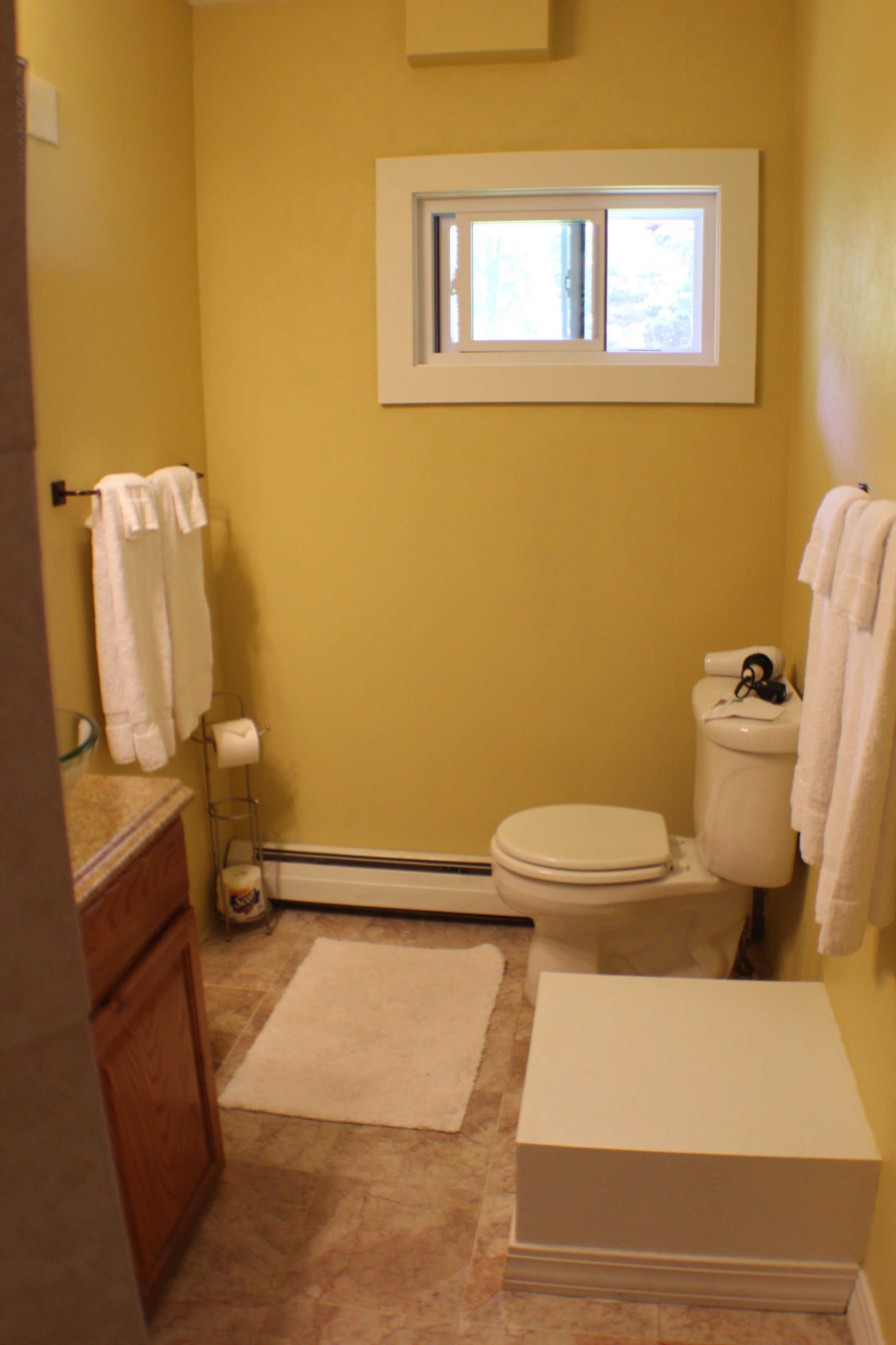 A compact bathroom with a toilet, a small window, a towel rack, and a glass shower enclosure.