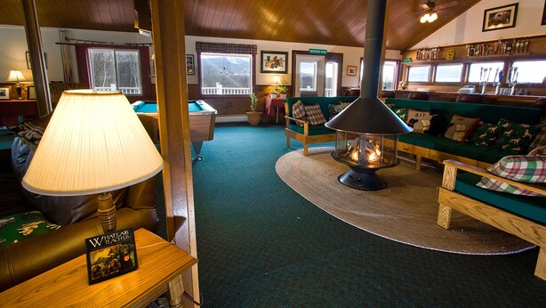 Une pièce chaleureuse avec une cheminée, des canapés verts, une table de billard et une lampe.