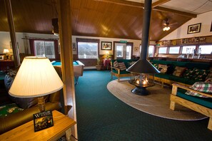A cozy room with a fireplace, green sofas, a pool table, and a lamp.