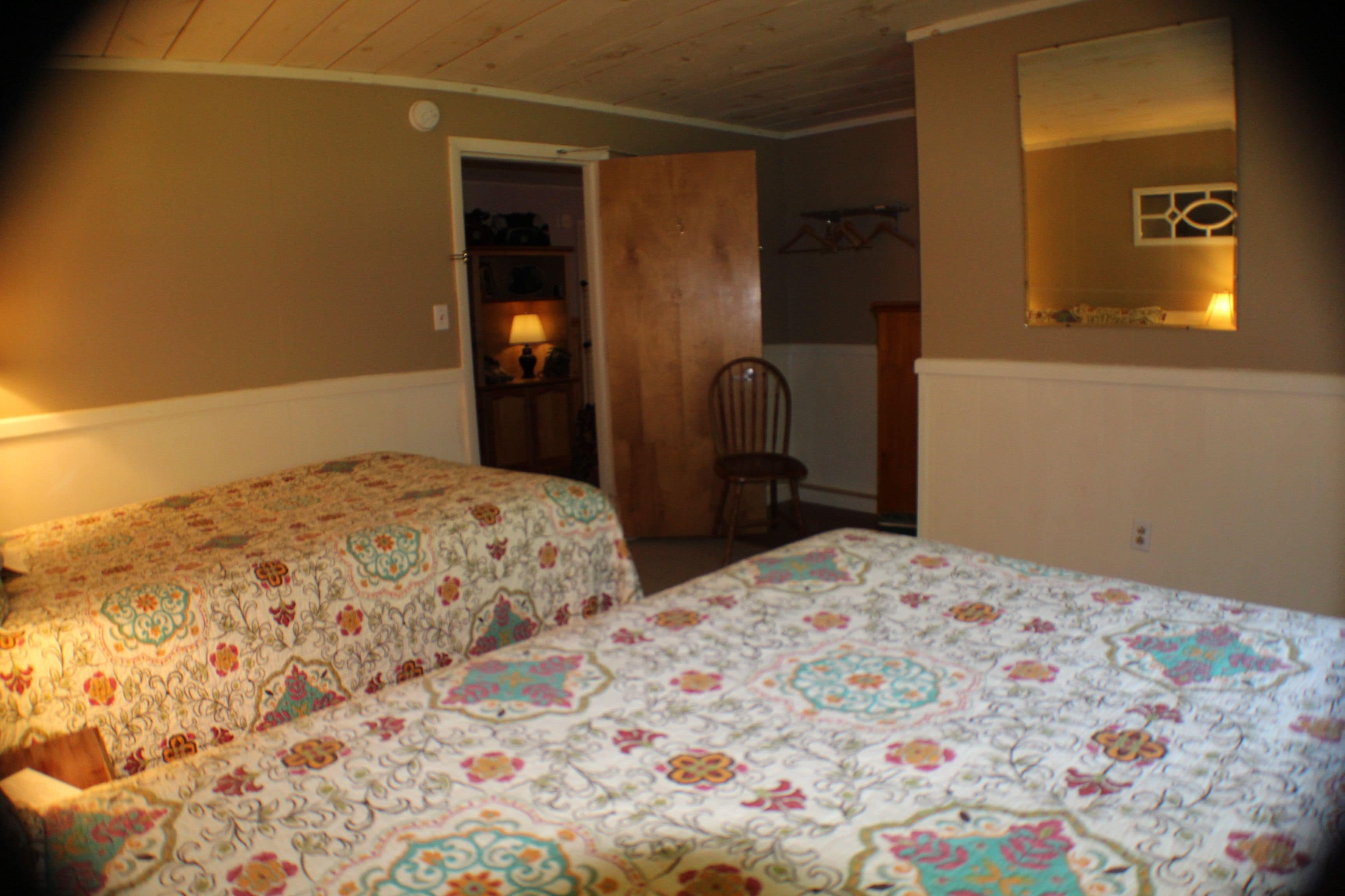 Ein Schlafzimmer mit zwei Betten, einem Sessel, einer Tür zu einem Badezimmer und einem Spiegel an der Wand.
