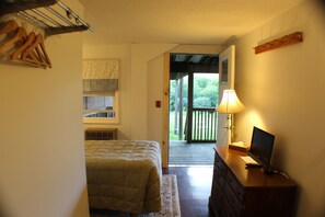 A bedroom with a bed, dresser, TV, and a view of a deck and greenery outside.
