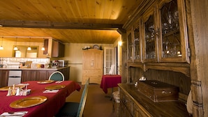Un intérieur en bois comprenant une table à manger pour quatre personnes, un buffet en bois avec des portes en verre et un coin cuisine équipé d’un réfrigérateur et de placards.