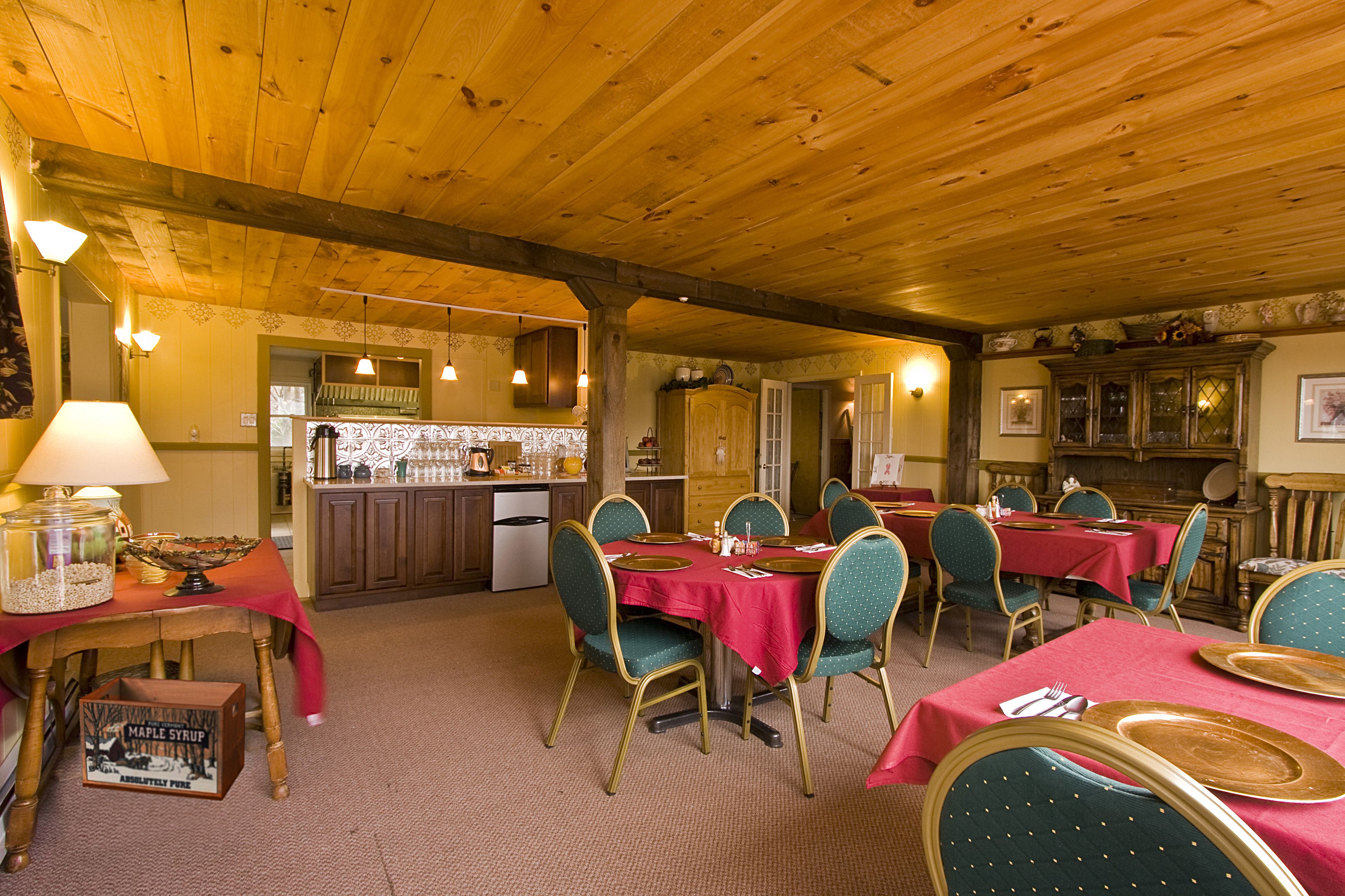 A dining area with wooden ceiling beams, red tablecloths, and green upholstered chairs.