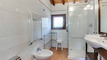 A bathroom with white tiles, a glass shower enclosure, a sink, and a bidet.