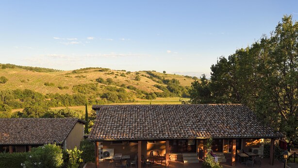Une villa avec un toit en tuiles, un espace extérieur aménagé et une vue sur des collines ondoyantes.