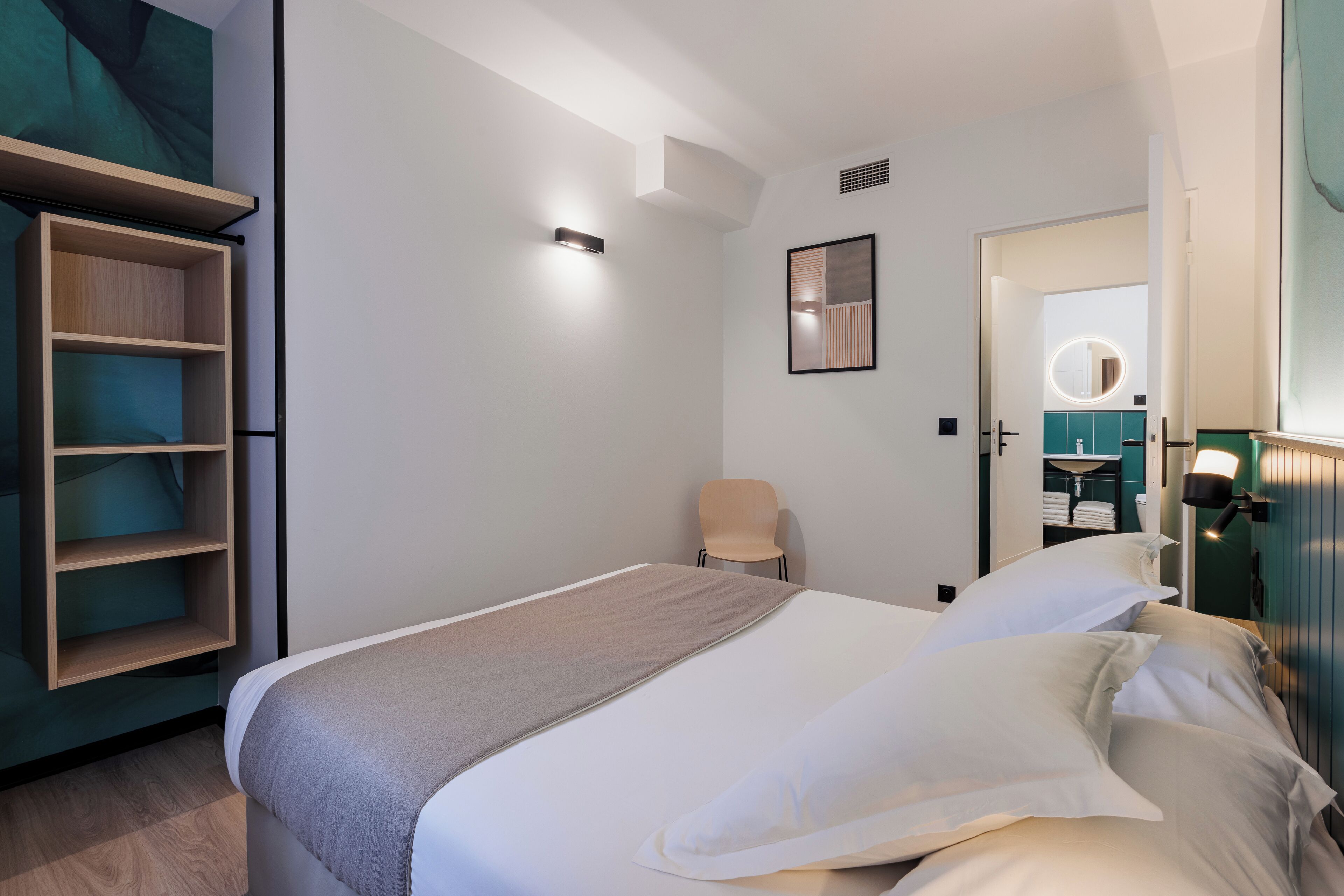 Una habitación de hotel moderna con una cama bien hecha, una silla y un armario con estantes.