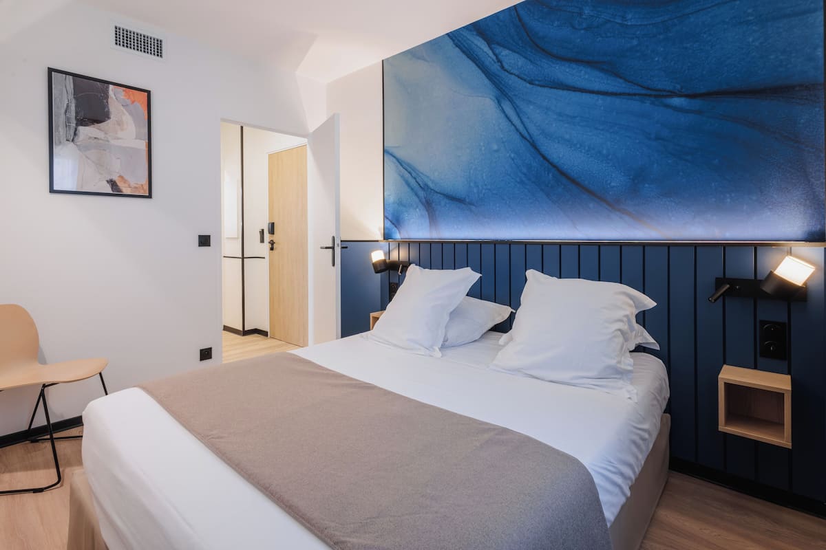 A modern hotel room with a large bed, a seating area, and a wall-mounted artwork.