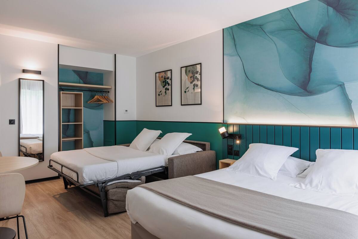 A hotel room with two beds, a desk, a chair, a wardrobe, and a large abstract painting on the wall.