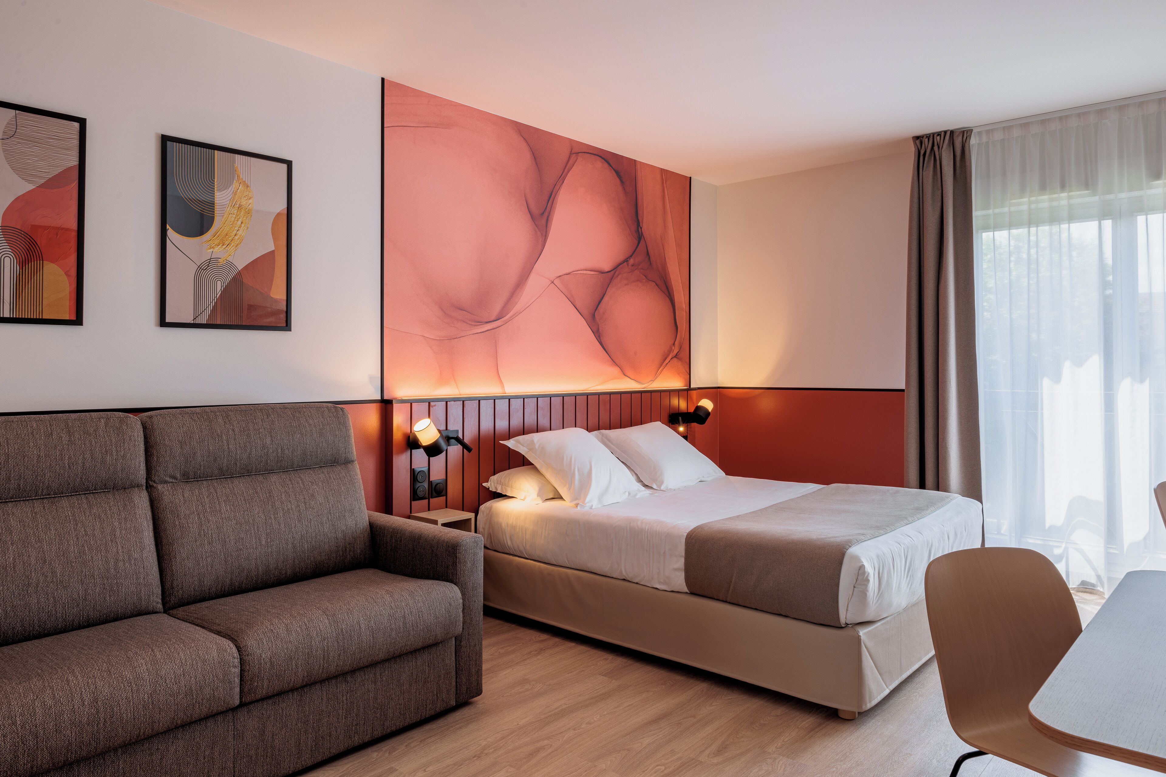 A modern hotel room with a sofa, a bed, a desk, and artwork on the walls.