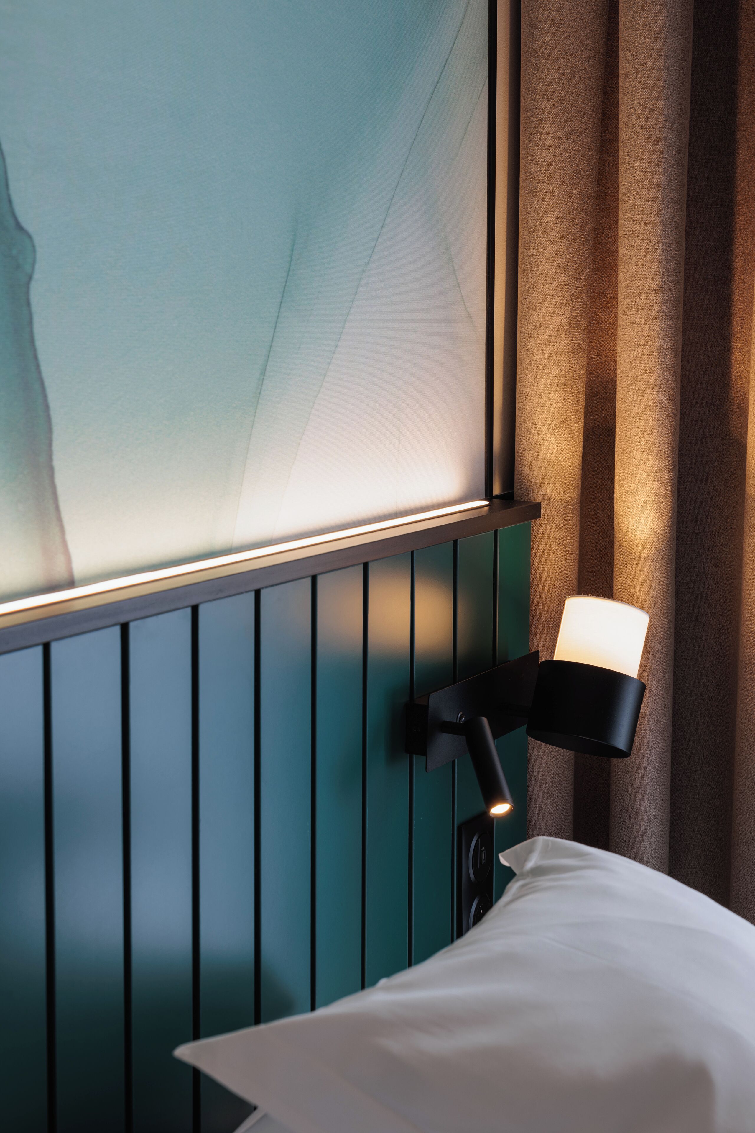 A neatly made bed with a white pillow and a black bedside lamp.