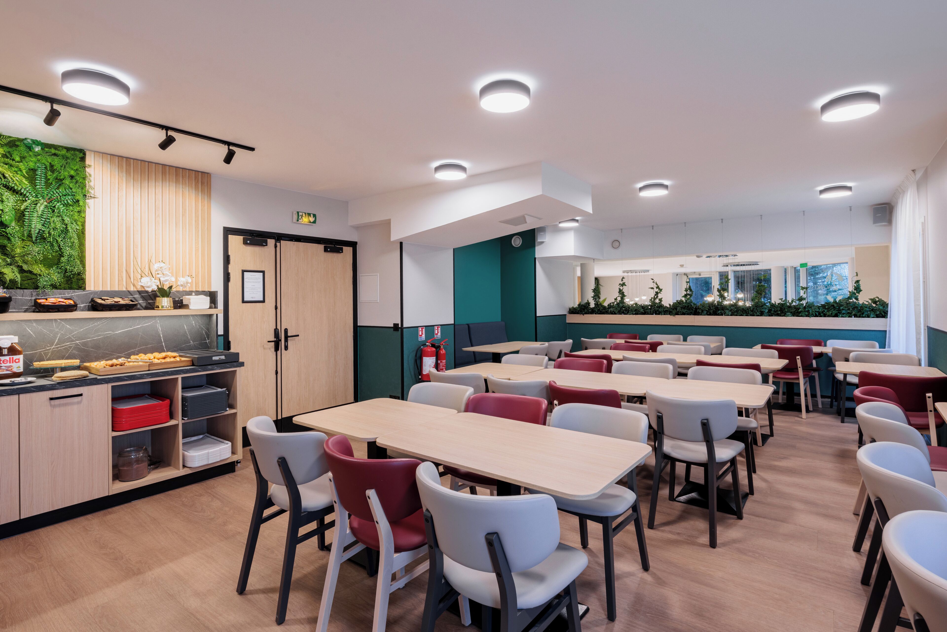 Una cafetería moderna con armarios de madera, una pared verde y diversas opciones de asientos, incluyendo mesas y sillas.