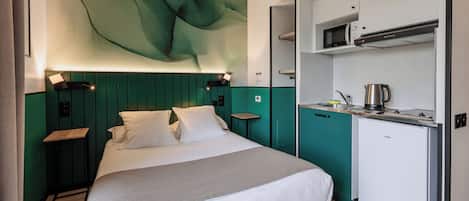 A hotel room with a bed, a small kitchenette, and a wall-mounted artwork.