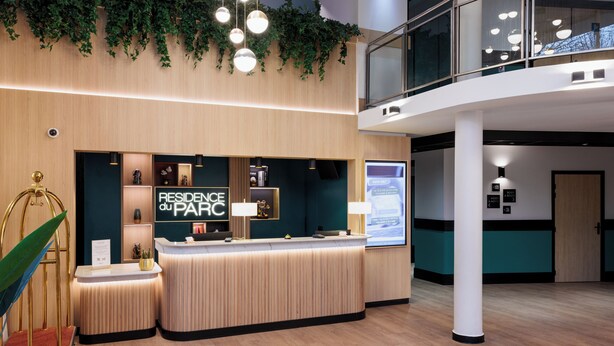 En moderne receptionsdisk med træfinish, en digital skærm og et skilt, der står 'RESIDENCE at PARC'.