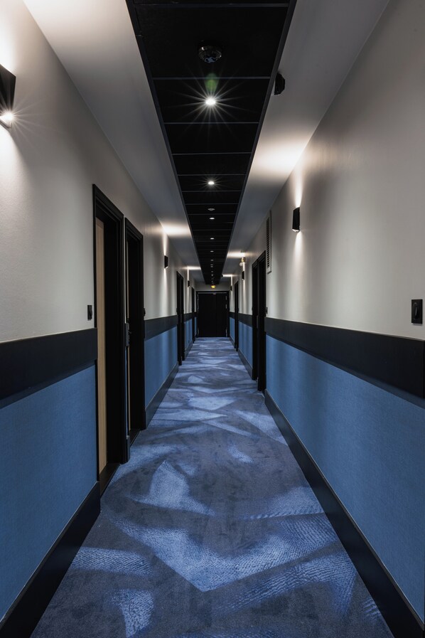 Un pasillo largo y estrecho con alfombra estampada, paredes en dos tonos y puertas a ambos lados.