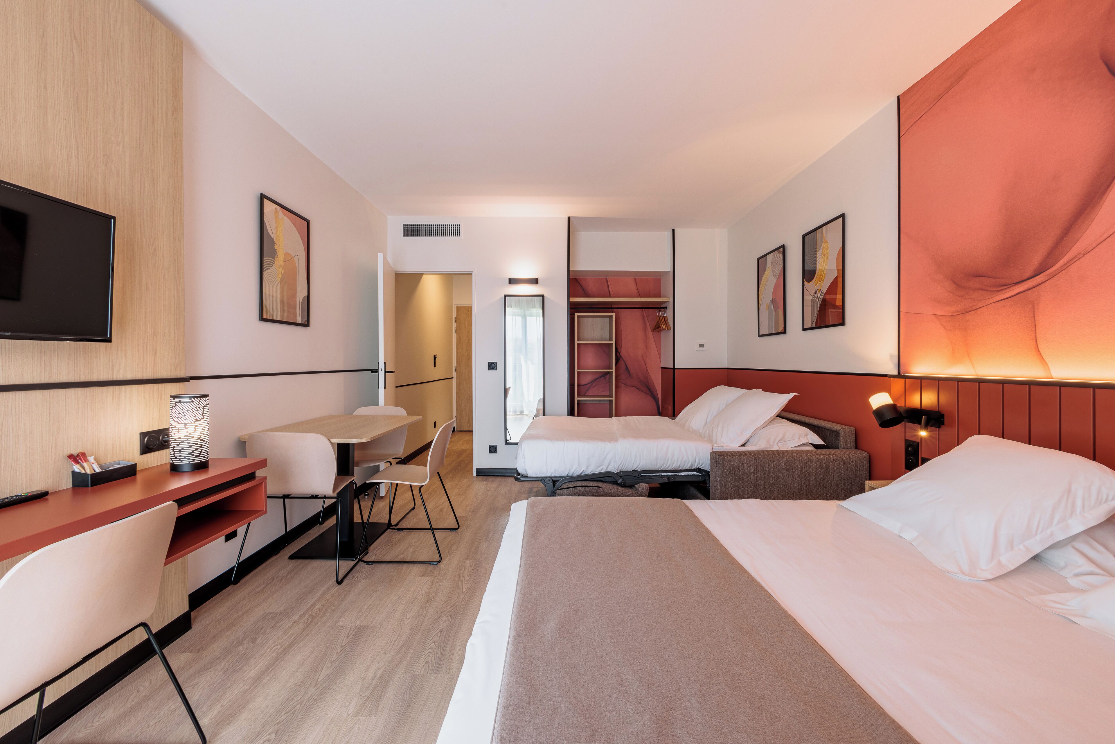 A hotel room with a bed, desk, chair, and a TV.