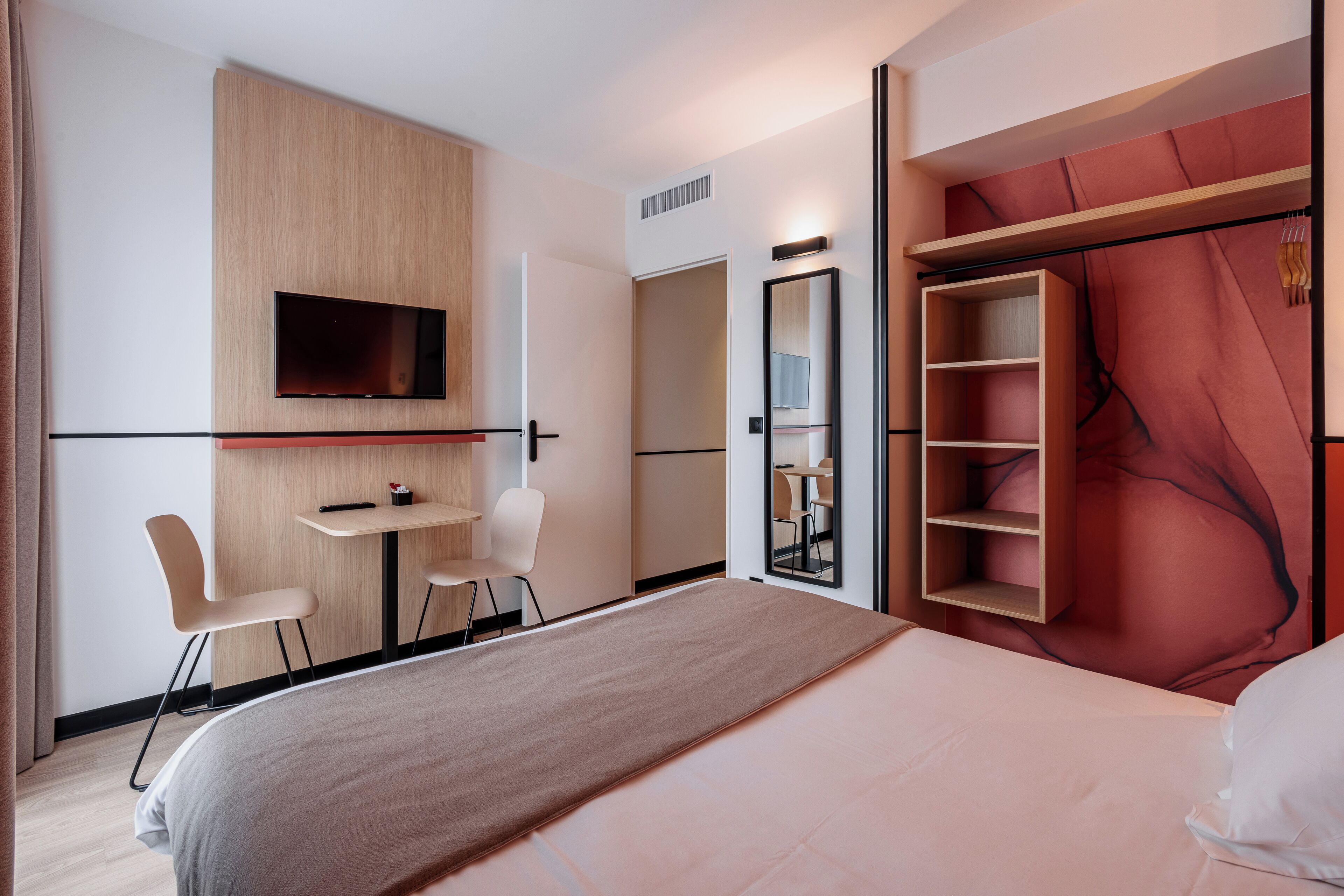 A modern hotel room with a bed, a desk, a chair, a TV, and a wardrobe.