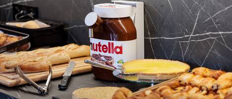 Un buffet proposant diverses pâtisseries, un pot de Nutella et des ustensiles disposés sur un plan de travail en marbre.