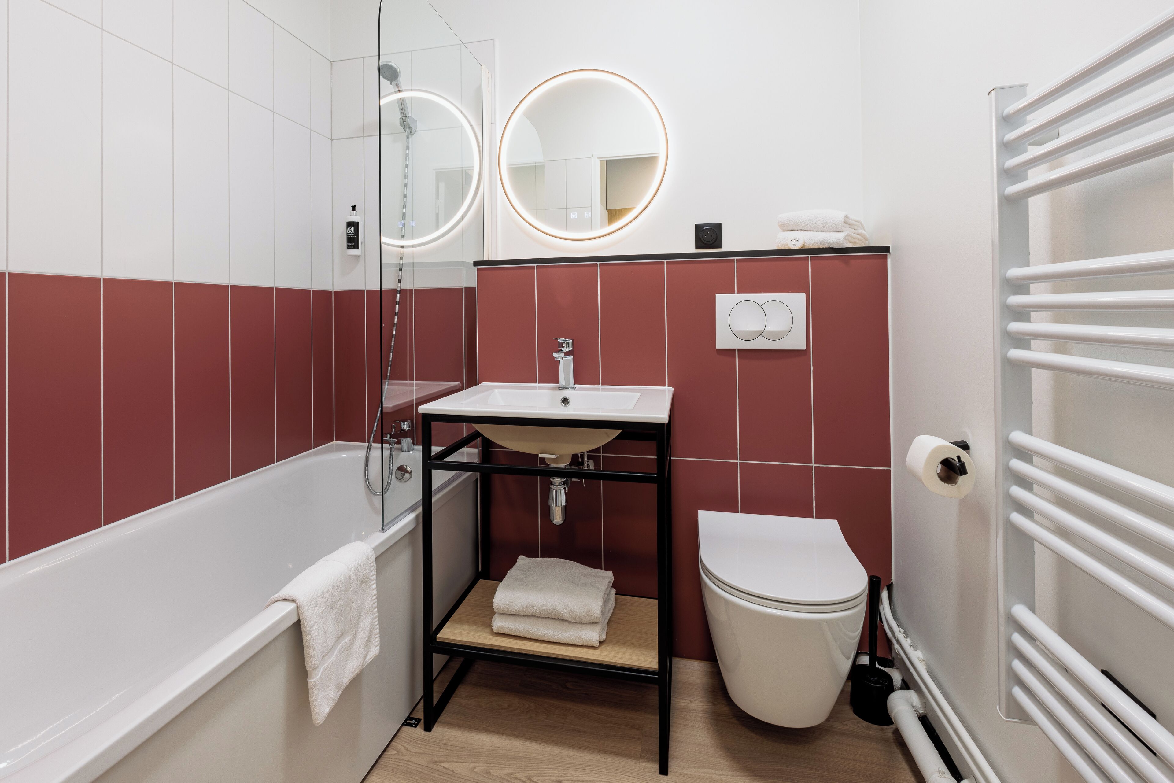 Un baño moderno con bañera, inodoro, lavamanos con espejo y un perchero para toallas.