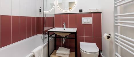 Un baño moderno con bañera, inodoro, lavamanos con espejo y un perchero para toallas.