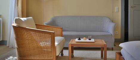 A room with a wicker chair, a striped sofa, a small table with a tray of items, and two floor lamps.