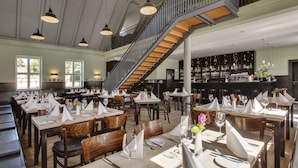 A restaurant with multiple dining tables set for guests, a staircase, and a bar area with shelves of bottles.