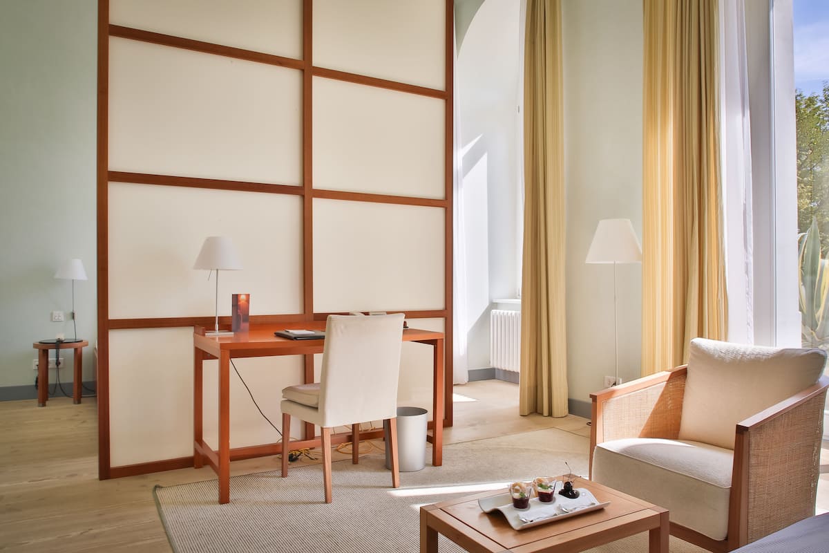 Una habitación de hotel moderna con un escritorio de madera, un sillón cómodo y vistas al exterior.