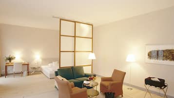 Una sala moderna con un sofá modular, dos sillones, una mesa de centro y una mesita auxiliar. Se ve un ventanal con vistas al horizonte de la ciudad.