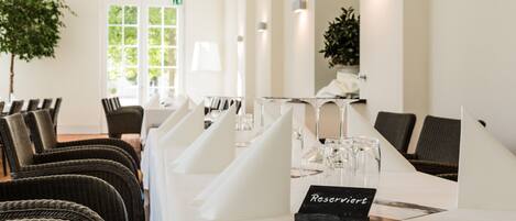 A hotel dining room with a long table set for a meal, wicker chairs, and a sign indicating a reserved table.