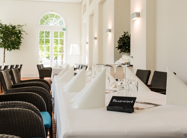 A hotel dining room with a long table set for a meal, wicker chairs, and a sign indicating a reserved table.