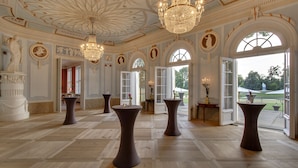 A grand room with ornate ceiling, chandeliers, and classical statues.