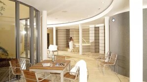 A modern indoor space with a curved ceiling, a seating area with tables and chairs, and a person in white attire walking in the background.
