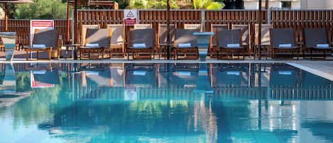A swimming pool with lounge chairs and umbrellas, surrounded by a wooden fence and greenery.